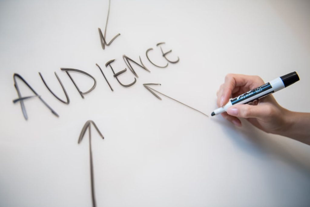 A person drawing an arrow pointing to the word “audience” on a whiteboard.